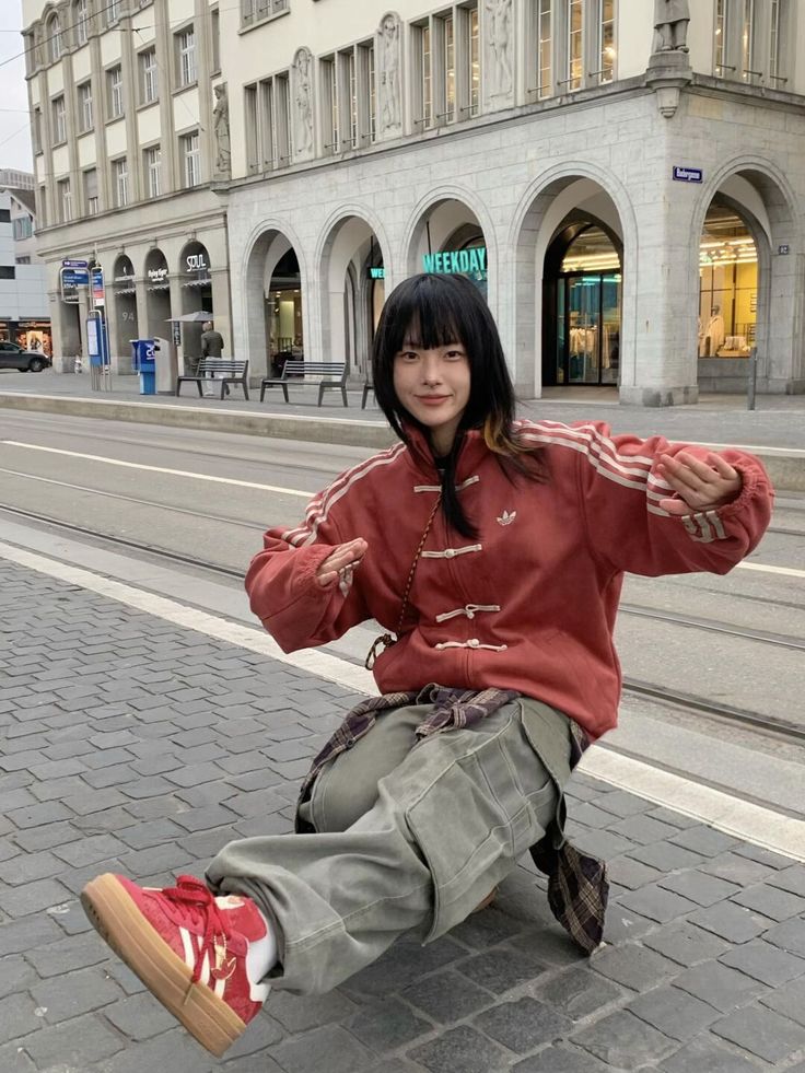 Person in a red cny jacket and green pants posing on a city street 
